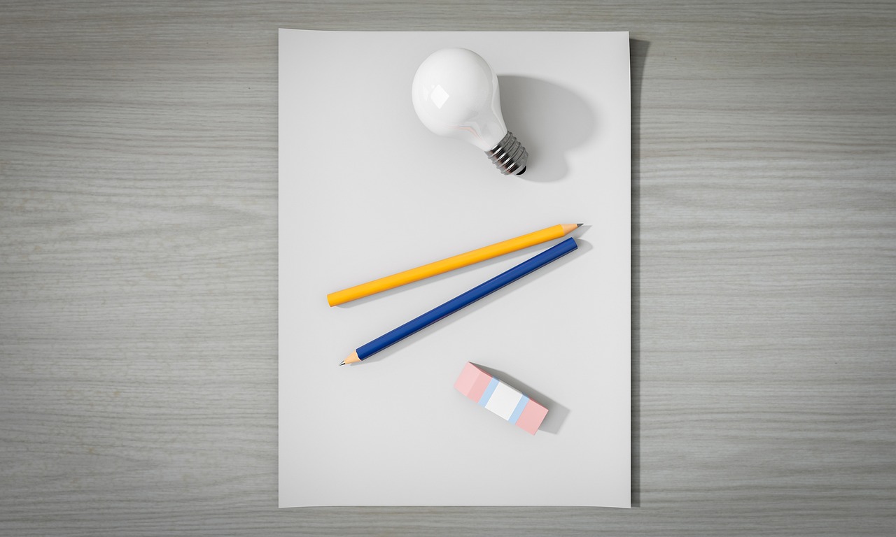 紙の上に鉛筆2本と電球1つ、消しゴム1個が置かれている